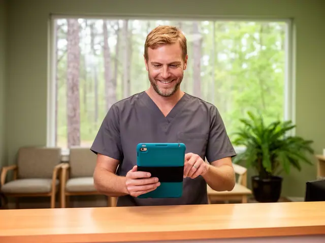 Dental practice office manager in charcoal scrubs smiling at a tablet behind a maple reception counter